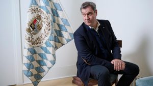 Markus Söder sitzend neben einer bayrischen Flagge
